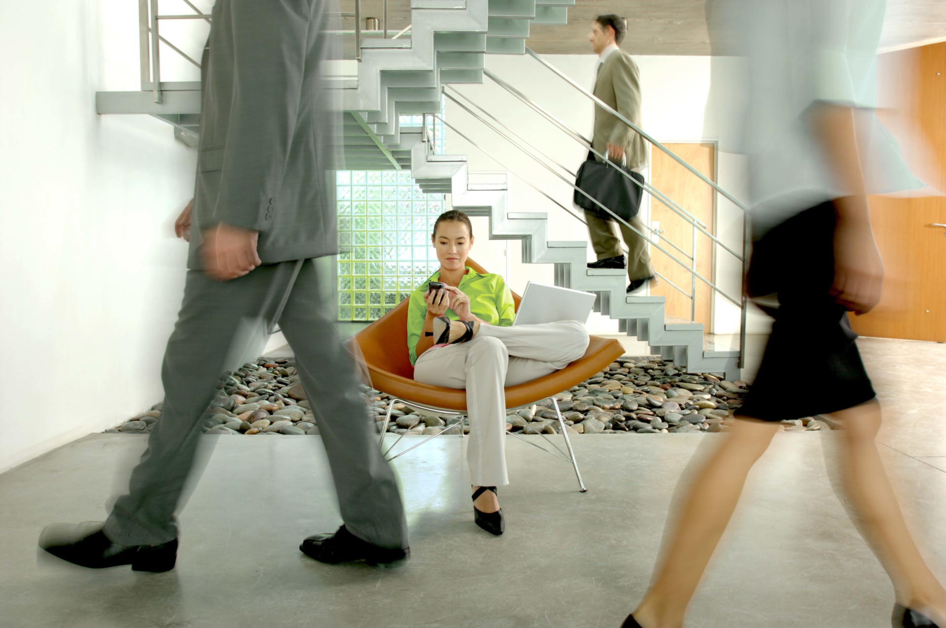 Businesswoman sitting on chair with laptop while colleagues walking on floor